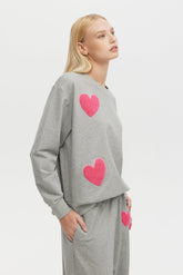 Woman wearing a gray sweatshirt with pink hearts on a white background