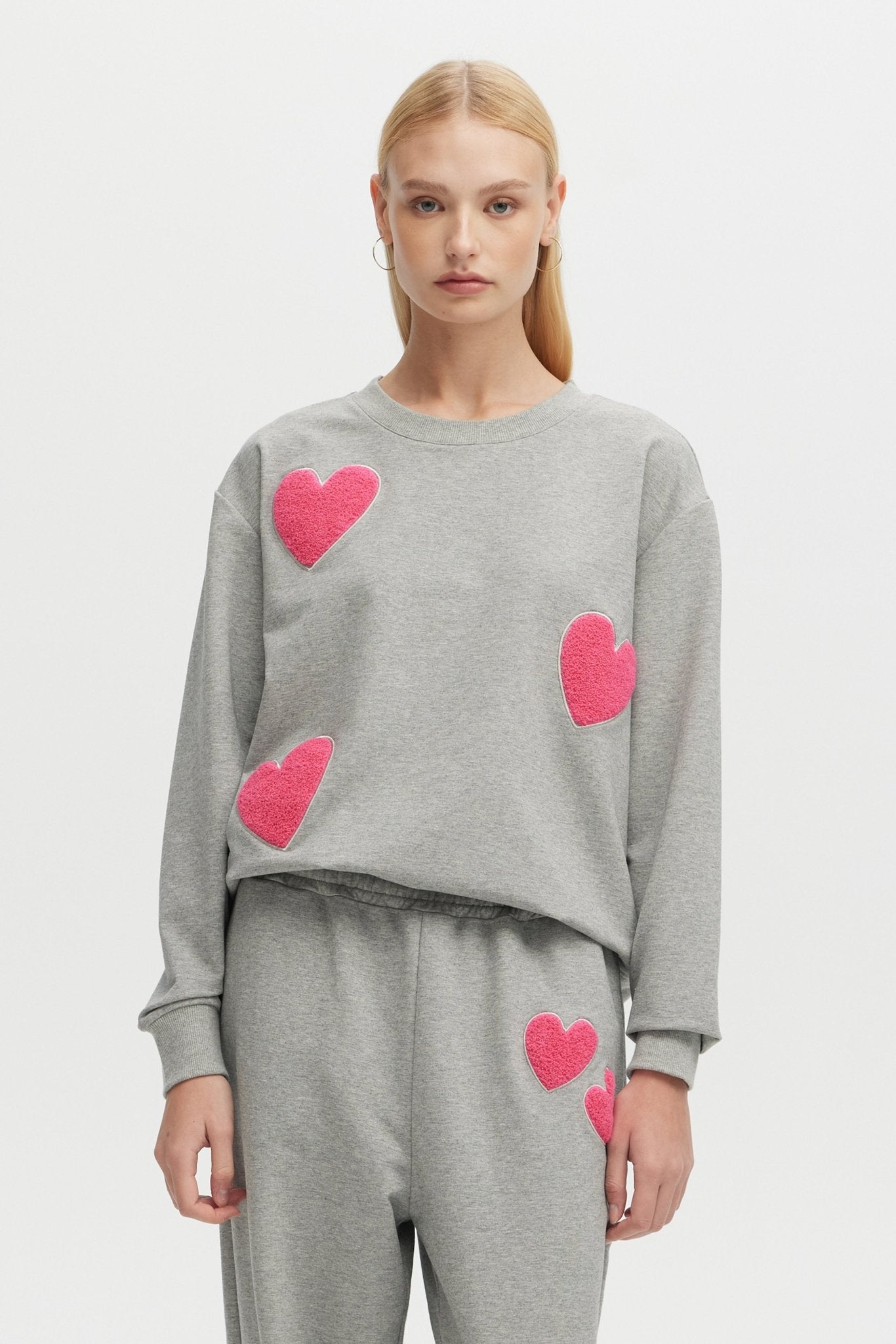 Person wearing a gray sweater with pink heart patterns on a light gray background