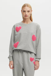 Person wearing a gray sweater with pink heart patterns on a light gray background