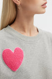 Gray sweatshirt with a pink heart patch worn by a person