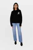 Woman wearing a black sweater with a star design and light blue jeans on a white background