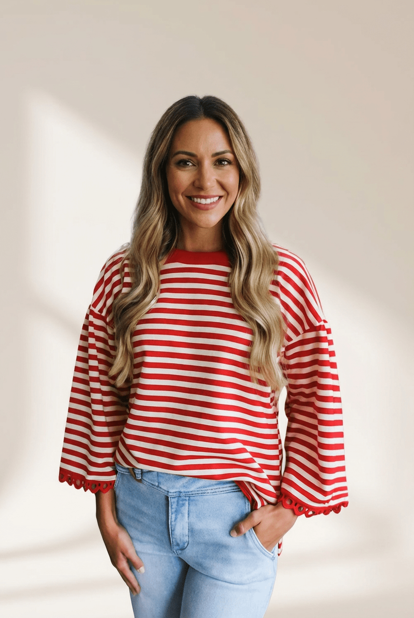 Woman wearing a red and white striped sweater with light blue jeans against a beige background