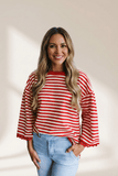 Woman wearing a red and white striped sweater with light blue jeans against a beige background