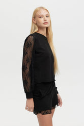 Woman wearing a black outfit with lace sleeves on a white background