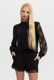 Woman wearing a black outfit with lace sleeves and shorts on a white background