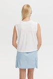 Woman wearing a white sleeveless top and light blue skirt on a plain background