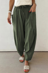 Person wearing olive green wide-leg pants with a white top and sandals on a neutral background