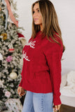 Woman in red cable-knit “Santa Santa” sweater with light blue jeans by Christmas tree.