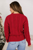 Back view of woman in red cable-knit sweater and light blue jeans by Christmas tree.