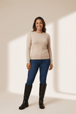 Woman wearing a beige sweater, blue jeans, and black boots on a beige background