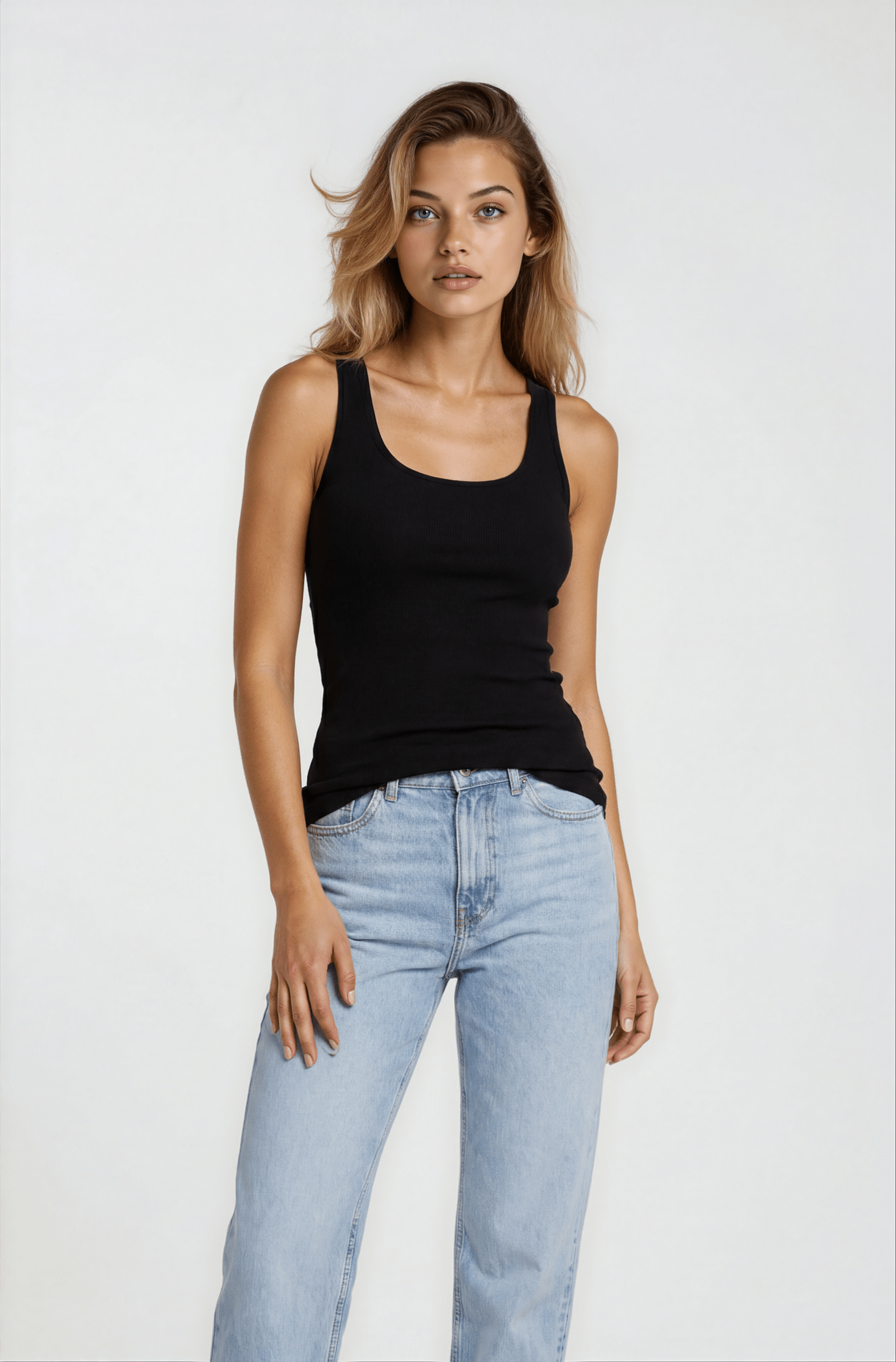Woman wearing a black tank top and light blue jeans on a white background