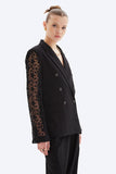 Black blazer with lace sleeves worn by a model on a white background