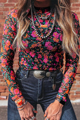 Person wearing a colorful floral long-sleeve top and dark jeans with a brick wall background.