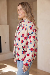 Woman in cream floral sherpa jacket with black trim and light blue jeans.