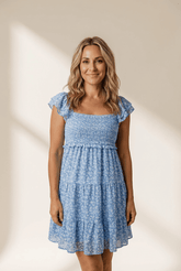 Woman wearing a blue floral dress against a plain background