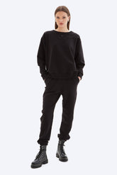 Person wearing a black outfit with black boots on a white background