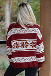 Woman seen from behind in burgundy and cream Fair Isle snowflake knit sweater by wooden post.
