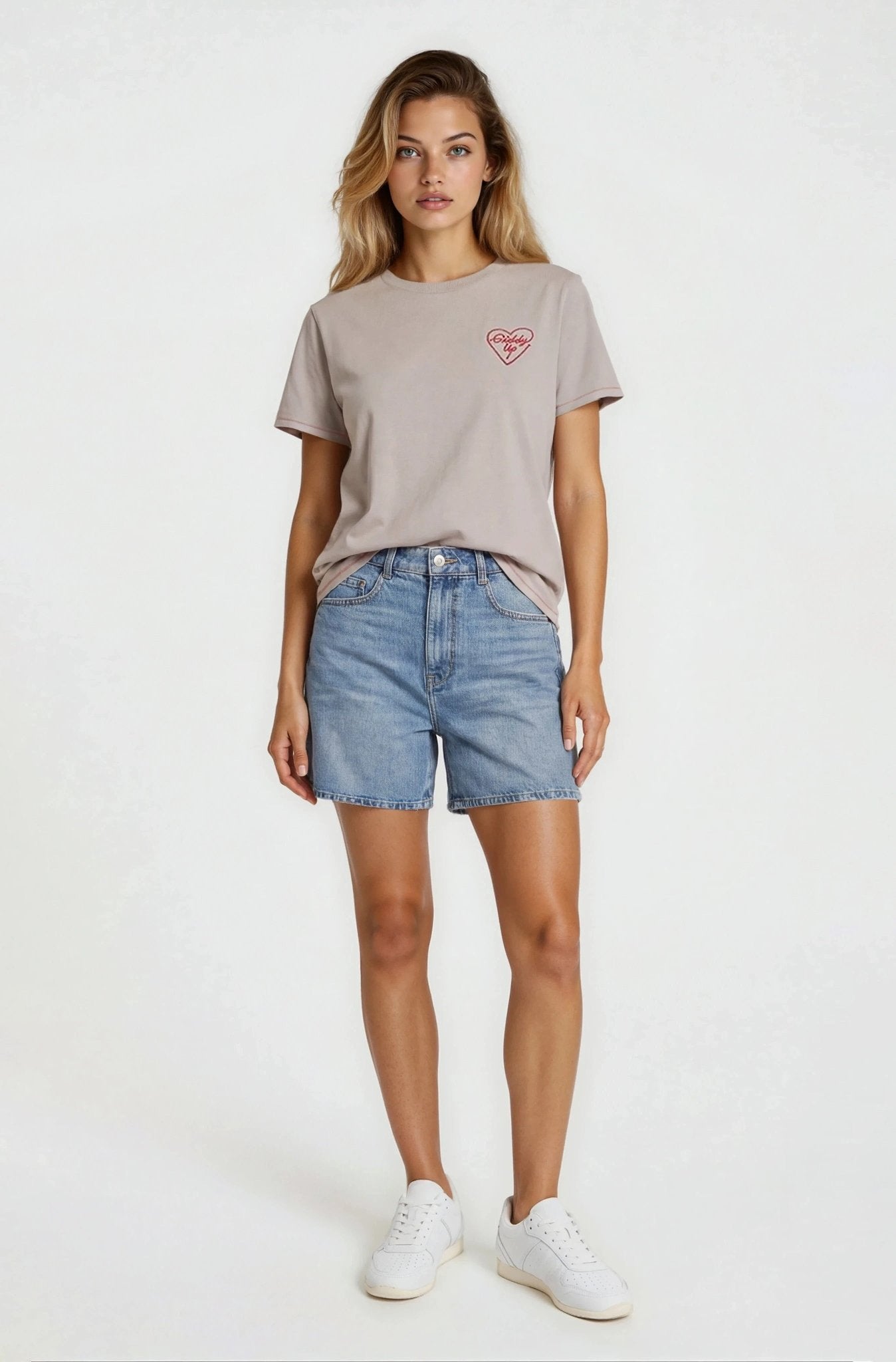 Woman wearing a gray t-shirt with a logo and denim shorts on a white background