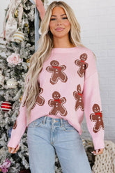 A woman wearing a pink knit sweater with brown gingerbread men patterns and red bow ties, paired with light blue jeans.