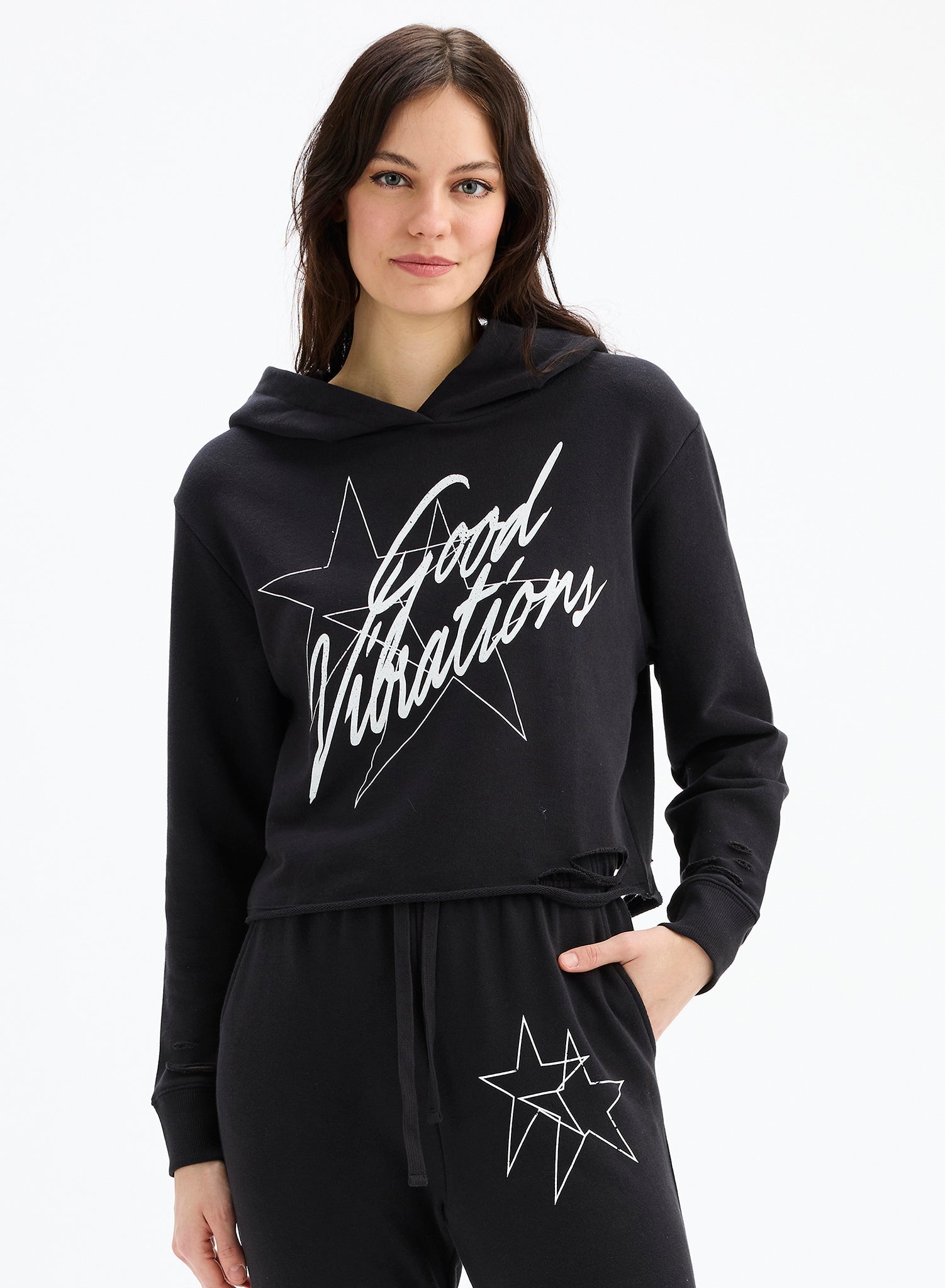 Woman wearing a black hoodie with 'Good Vibrations' text and star design on a white background