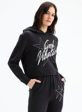Woman wearing a black hoodie with 'Good Vibration' text and star design on a white background