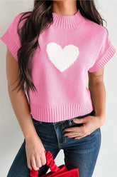 Person wearing a pink sweater with a white heart design on a plain background