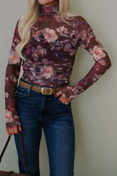 Person wearing a floral long-sleeve top and blue jeans against a plain background