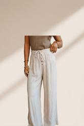 Person wearing a beige top and white pants against a neutral background