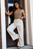Woman in a brown top and white pants standing in a doorway.