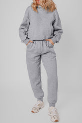 Model in light gray heathered sweatshirt and joggers with beige sneakers.