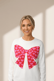 Woman wearing a white sweater with a pink heart bow design on a beige background