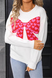 White sweater with a pink heart-patterned bow design worn by a person.