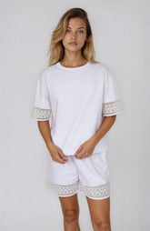 Woman wearing a white outfit with lace details on a plain background