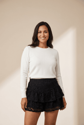 Woman wearing a white sweater and black layered skirt against a beige background