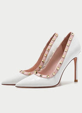 White high-heeled shoes with gold studded details on a light gray background