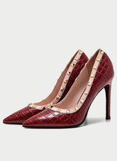 Red high-heeled shoes with gold studded details on a light gray background