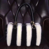 Black handbag with white fur tassels on a dark textured background