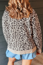Back view of person in beige knit sweater with dark leopard print and light blue ruffled shorts against wood.