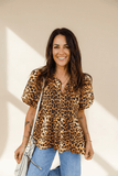 Woman wearing a leopard print blouse and blue jeans against a beige wall.