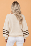 Woman wearing a cream knit sweater with leopard-print sleeves and white pants.