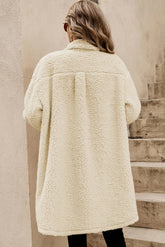 Person wearing a cream-colored sherpa coat standing on wooden steps.