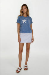 Woman wearing a blue t-shirt with a star design and a white skirt on a white background