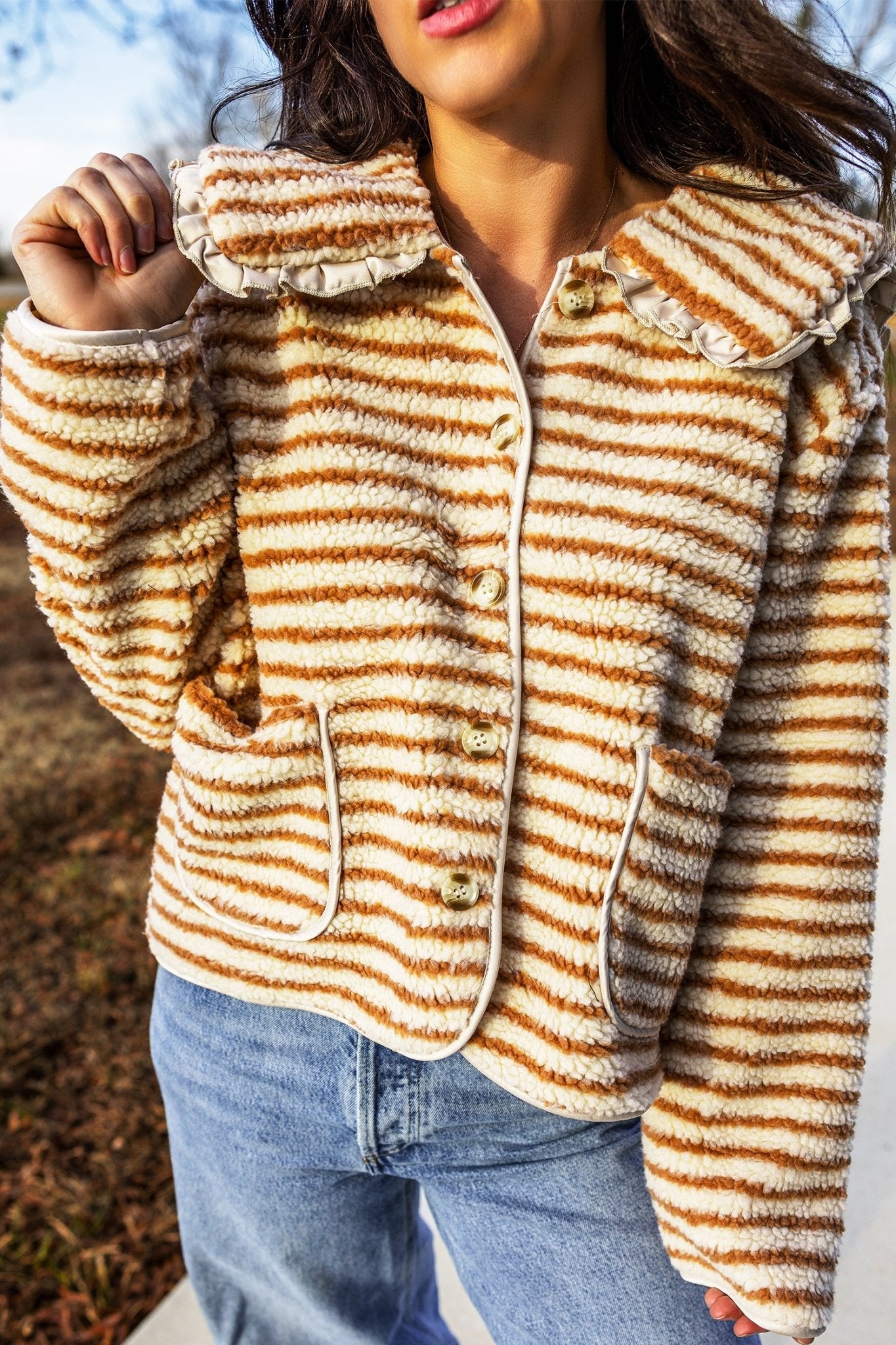 Woman in fuzzy striped cropped jacket with ruffled collar and blue jeans.