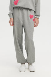 Person wearing gray sweatpants with pink hearts on a white background