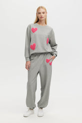 Woman wearing a gray sweatshirt and pants with pink heart designs on a white background
