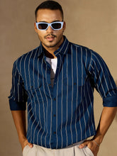 Man wearing a blue pinstripe shirt and sunglasses against a beige background