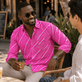 Man in a pink shirt holding a coffee cup, sitting outdoors with another person.