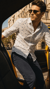 Man in a patterned shirt and sunglasses getting out of a taxi in an urban setting