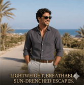 Man wearing sunglasses and a gray shirt standing on a sun-drenched path with palm trees and ocean in the background.