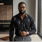 Man wearing a black patterned shirt and glasses indoors